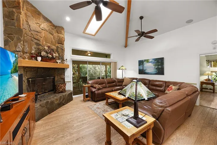 Living room featuring wood-type flooring, a ceiling fan, vaulted ceiling, and a stone fireplace