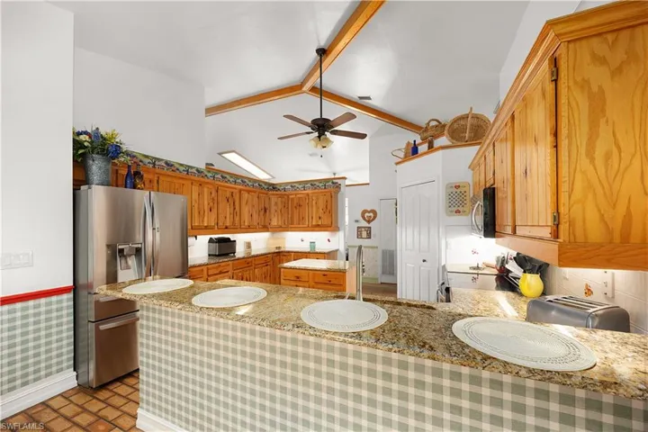 Kitchen with stainless steel appliances, wood finish cabinets, a ceiling fan, a peninsula, and light stone counters