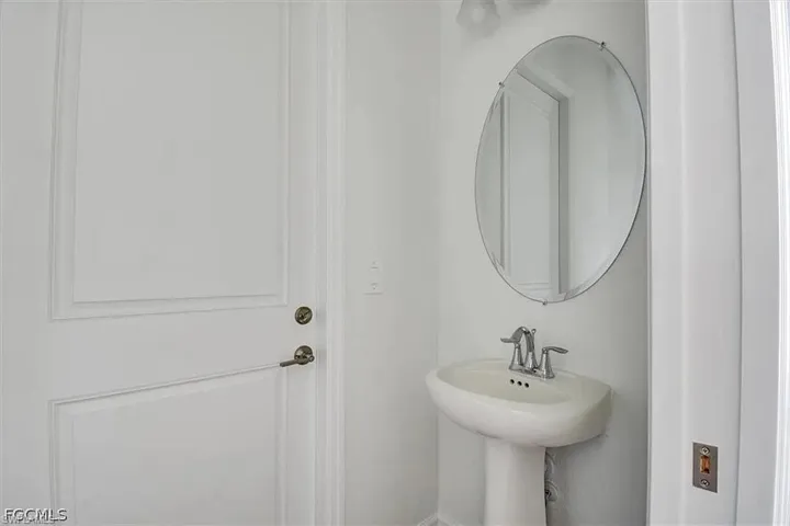 Pedestal sink with chrome faucet, complemented by an oval frameless mirror and white paneled door with brushed nickel hardware