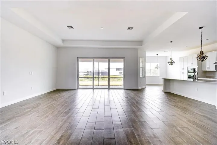 Expansive open-concept room featuring wood-finish tile flooring, tray ceiling, and sliding glass doors to the exterior