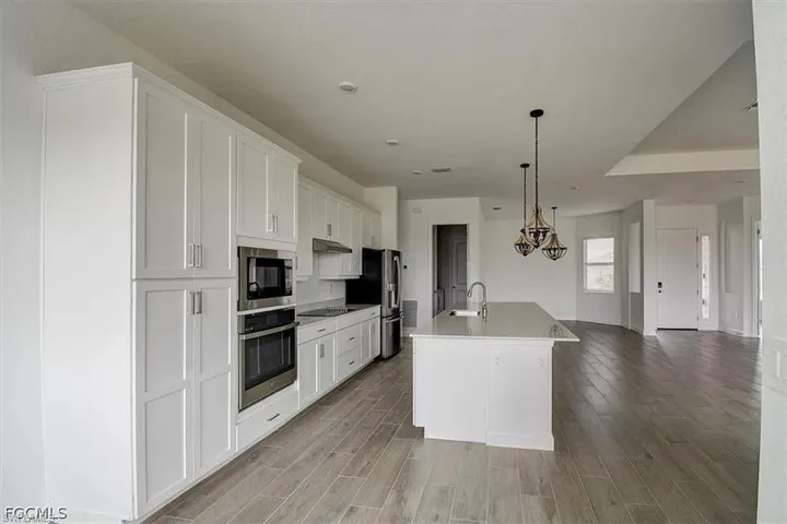 Modern kitchen featuring white cabinetry, stainless steel appliances, a central island with sink, and wood-finish flooring