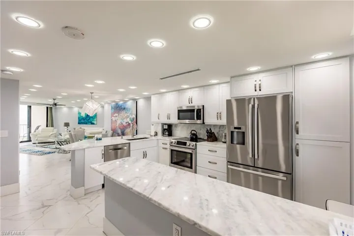 Kitchen featuring stainless steel appliances, a peninsula, open floor plan, white cabinetry, and light stone counters