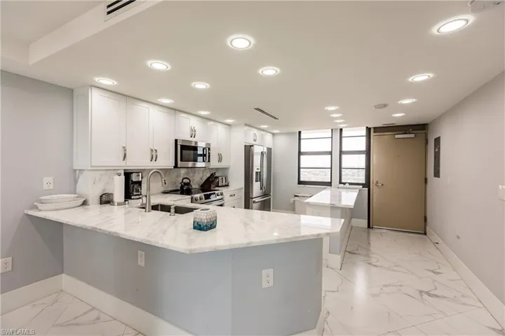 Kitchen featuring a center island, a peninsula, light stone counters, white cabinets, and stainless steel appliances