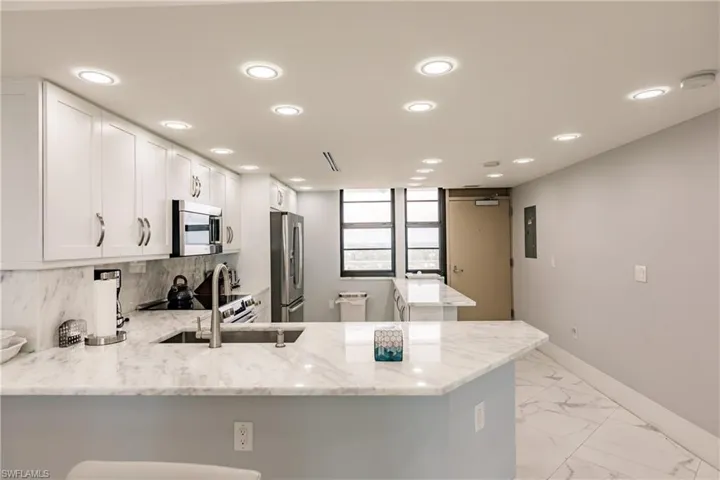 Kitchen featuring white cabinetry, a peninsula, light stone counters, a kitchen bar, and stainless steel appliances