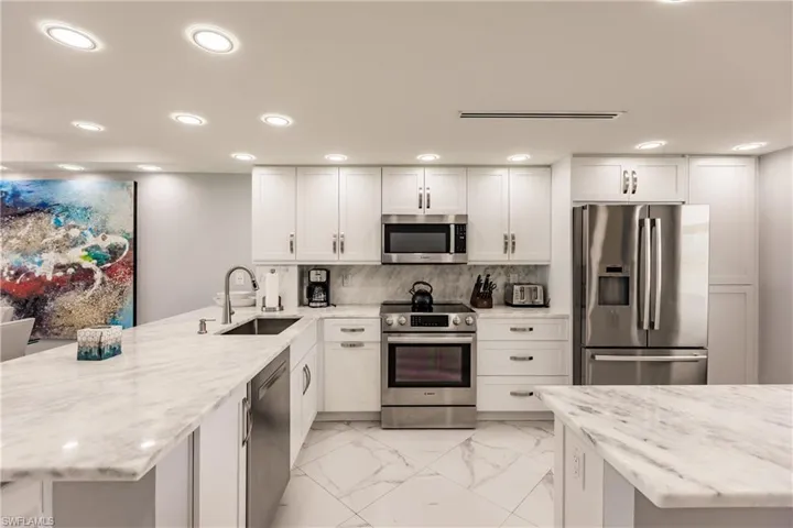 Kitchen featuring stainless steel appliances, a peninsula, white cabinetry, light marble finish floors, and light stone countertops