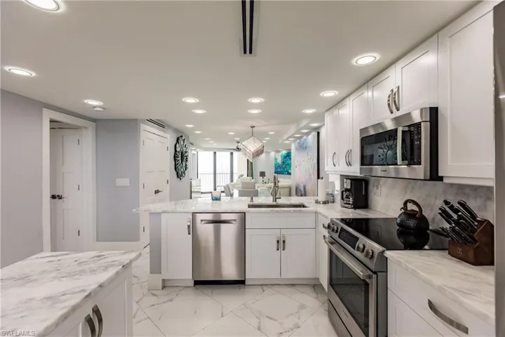 Kitchen featuring stainless steel appliances, a peninsula, white cabinets, and light stone countertops