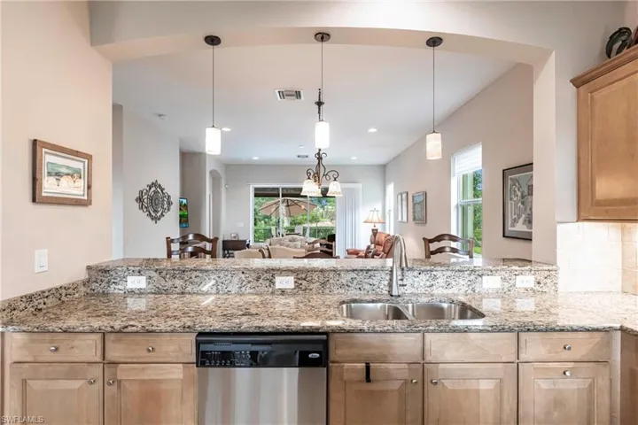 Kitchen with light stone countertops, arched walkways, dishwasher, and plenty of natural light