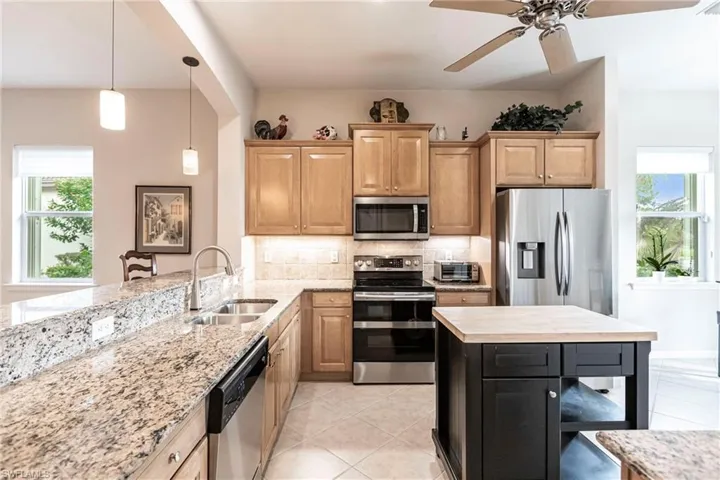 Kitchen with appliances with stainless steel finishes, light stone counters, pendant lighting, light tile patterned flooring, and a ceiling fan