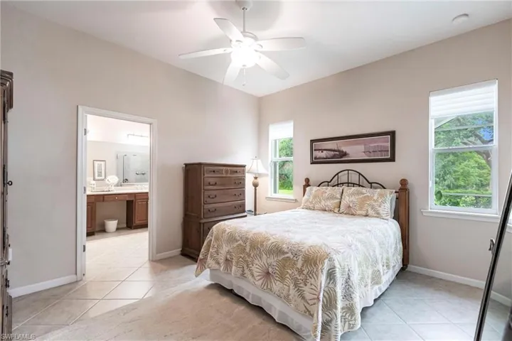 Bedroom featuring light tile patterned floors, ceiling fan, and ensuite bath