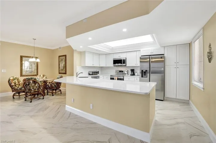 Kitchen with light marble finish flooring, white cabinetry, appliances with stainless steel finishes, crown molding, and hanging light fixtures