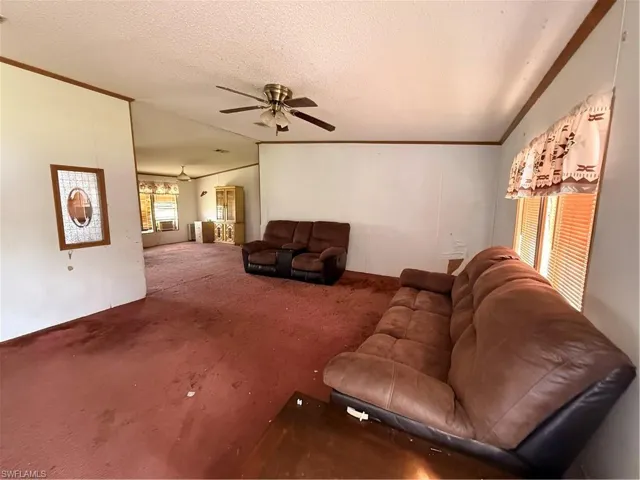 Living area featuring carpet flooring, a textured ceiling, crown molding, and a ceiling fan