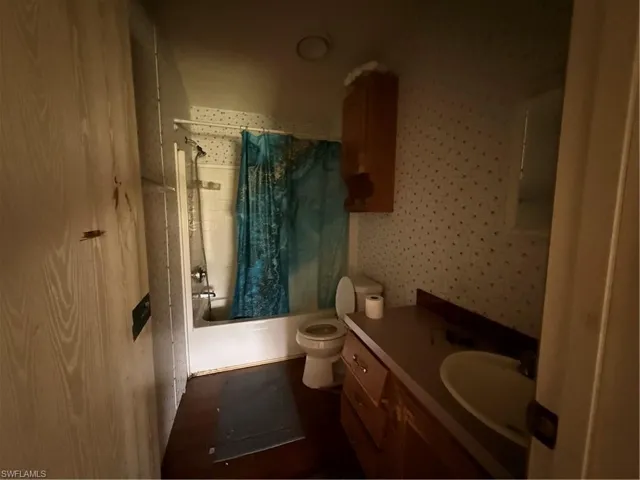 Full bathroom featuring shower / bath combo with shower curtain, vanity, and wallpapered walls