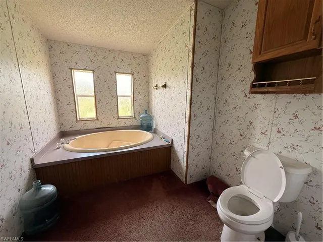 Bathroom featuring wallpapered walls, a garden tub, a textured ceiling, and carpet floors