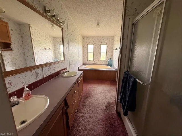 Full bathroom with double vanity, a stall shower, dark colored carpet, a bath, and wallpapered walls