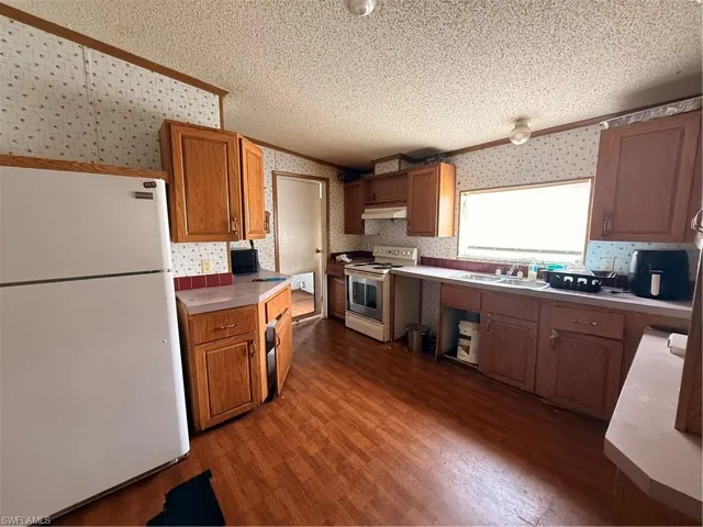 Kitchen with refrigerator, brown cabinets, wallpapered walls, dark wood-style floors, and light countertops