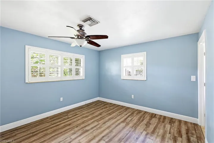 Room featuring wood-finish flooring, two windows with white plantation shutters, and a ceiling fan with light fixture