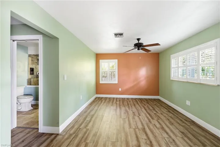Spacious room featuring wood-finish flooring, a ceiling fan, and two windows with white plantation shutters