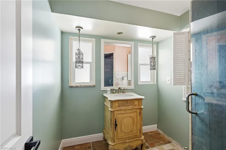 Bathroom featuring a decorative vanity with a marble countertop and undermount sink, dual pendant light fixtures, and a glass-enclosed shower