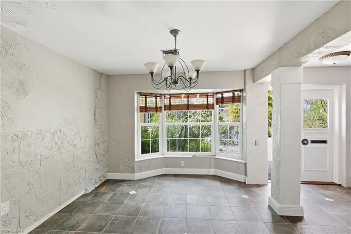 Tiled flooring featuring a bay window with natural light, a decorative chandelier, and textured wall finishes
