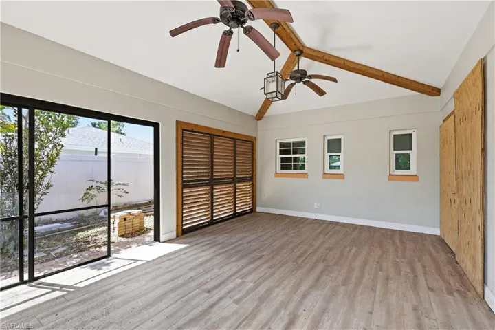 Spacious room featuring wood-finish flooring, exposed wood ceiling beams, and dual ceiling fans