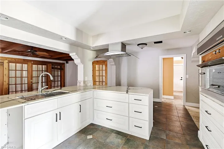 Kitchen featuring white cabinetry, a large kitchen island with a built-in sink, stainless steel range hood, and integrated double ovens