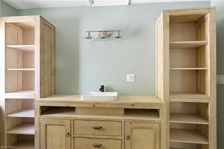 Built-in wood-finish vanity featuring a rectangular vessel sink with a matte black faucet, flanked by tall open shelving units, all under a brushed nickel three-light fixture