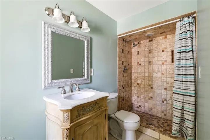 Bathroom featuring a decorative vanity with a white countertop and undermount sink, an ornate framed mirror, and a tiled shower stall with a built-in niche