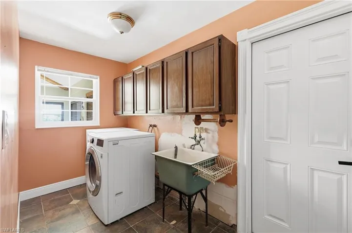 Utility room featuring tile flooring, a window with white trim, dark wood cabinetry, a utility sink, and a paneled interior door