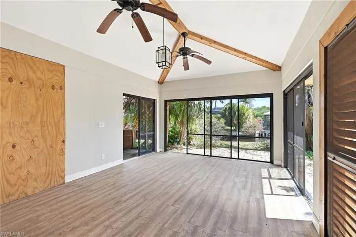 Expansive room featuring wood-finish flooring, vaulted ceiling with exposed wood beams, and dual ceiling fans