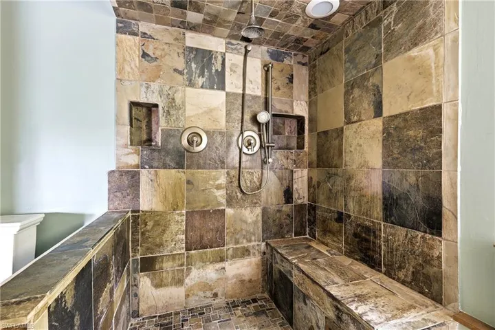 Spacious shower featuring multi-toned stone tile walls and ceiling, built-in bench, two recessed niches, and dual shower heads