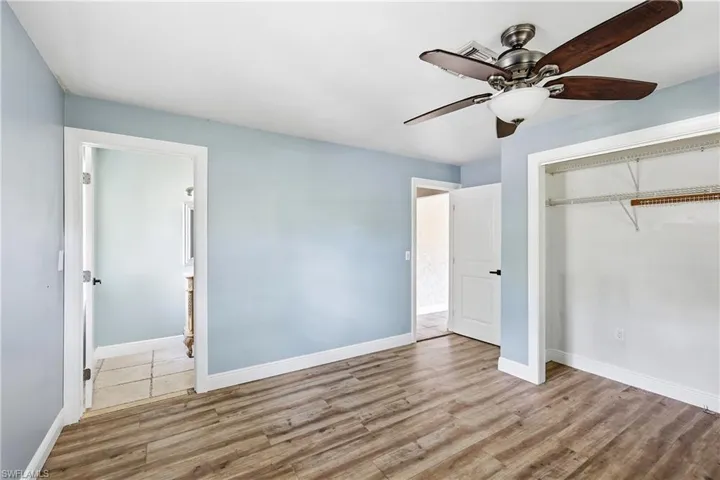 Room featuring wood-finish flooring, light blue walls, and a ceiling fan with dark wood-tone blades