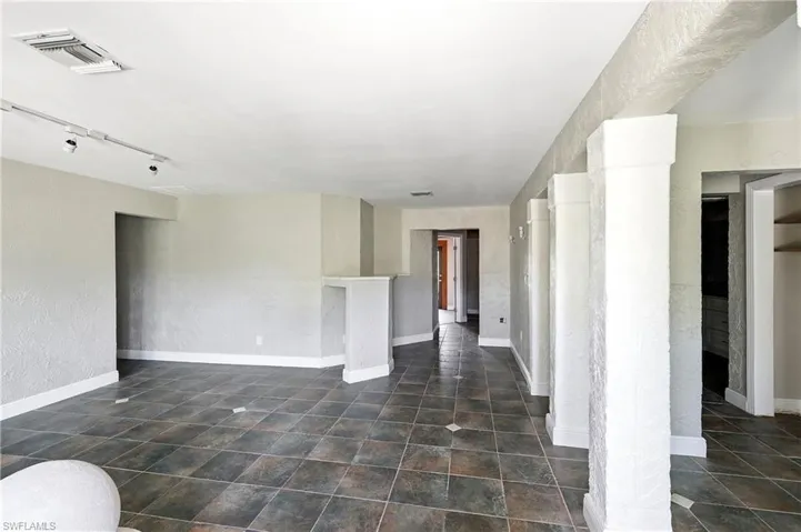 Spacious room featuring large format tile flooring, textured walls, track lighting, and architectural columns