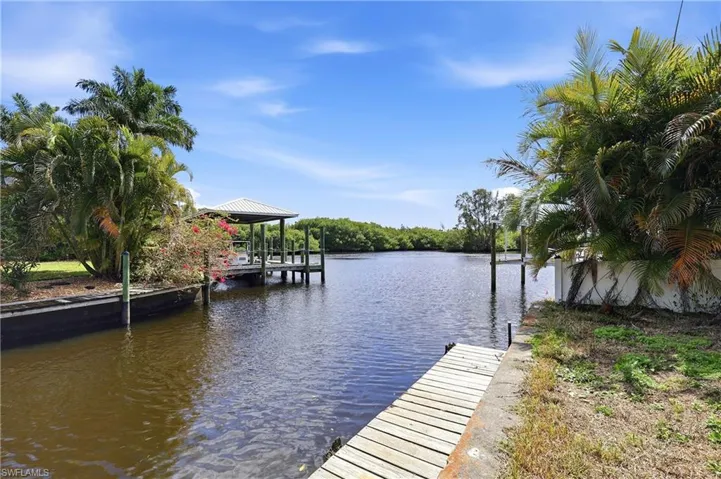 Waterfront property with a covered dock, additional wooden dock, lush tropical landscaping, and mature foliage