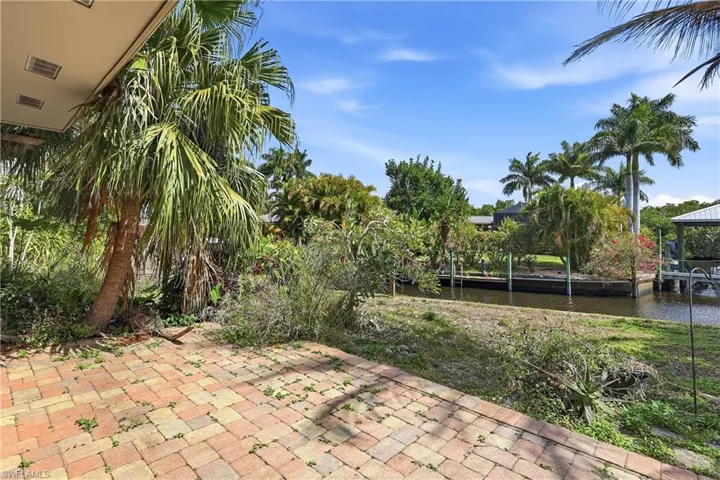 Brick paver patio and mature palm trees defining the outdoor area, with a canal and boat dock visible in the background