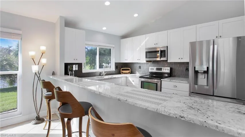 Kitchen featuring white cabinetry, light stone countertops, appliances with stainless steel finishes, and lofted ceiling