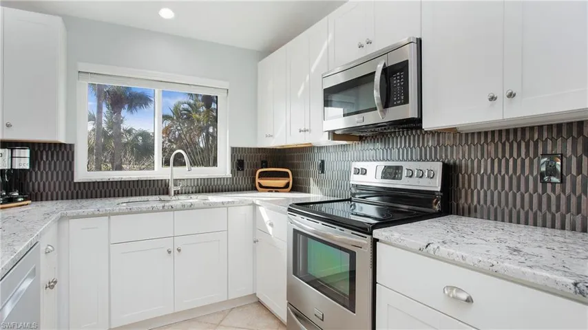 Kitchen with decorative backsplash, white cabinetry, and stainless steel appliances