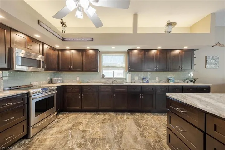 Kitchen with light tile patterned flooring, backsplash, light stone counters, ceiling fan, and stainless steel appliances