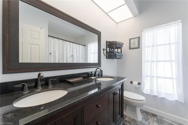 Bathroom with toilet, tile patterned floors, and double sink vanity
