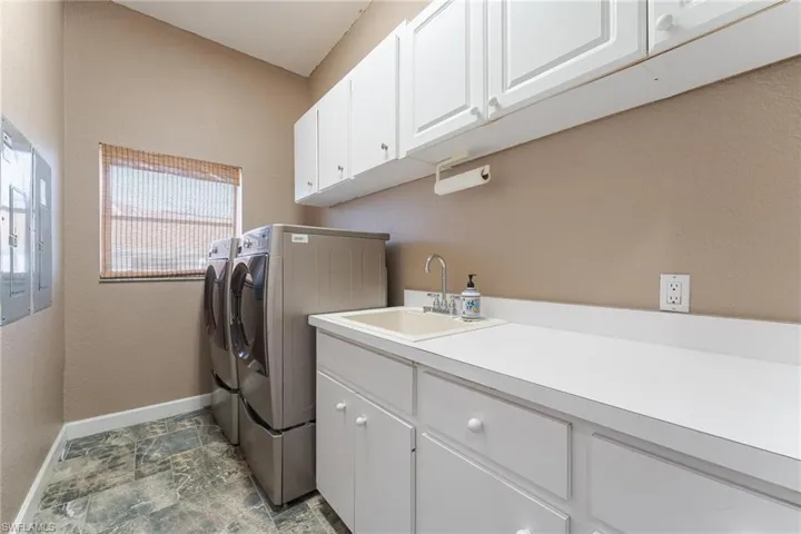 Laundry room with cabinets, dark tile patterned floors, washer and clothes dryer, and sink