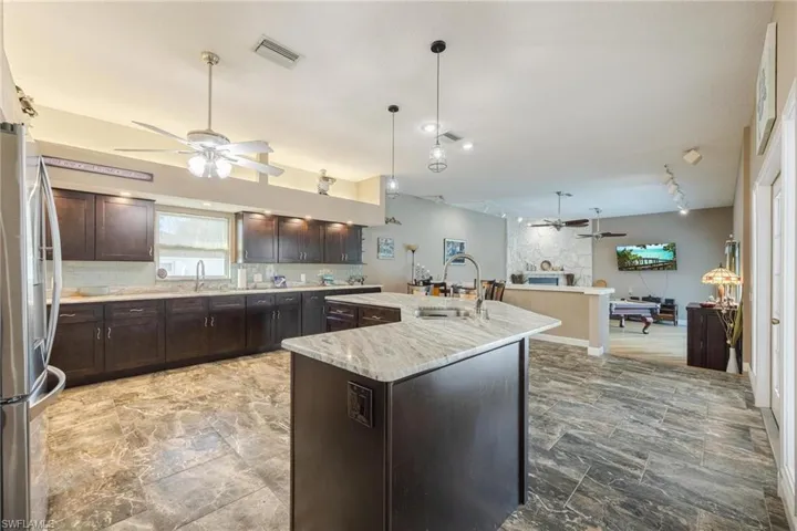 Kitchen featuring decorative light fixtures, ceiling fan, an island with sink, sink, and stainless steel refrigerator