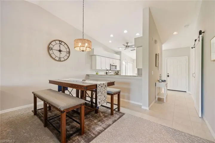 Dining area featuring vaulted ceiling, a barn door, a ceiling fan, light tile patterned flooring, and light colored carpet