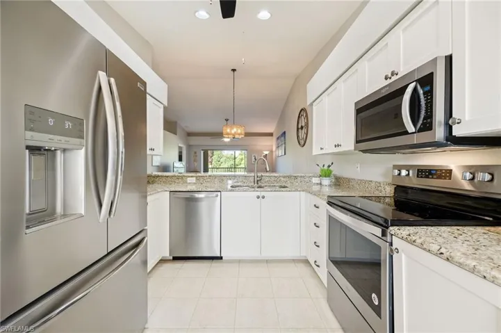 Kitchen featuring stainless steel appliances, vaulted ceiling, light stone countertops, white cabinets, and a ceiling fan