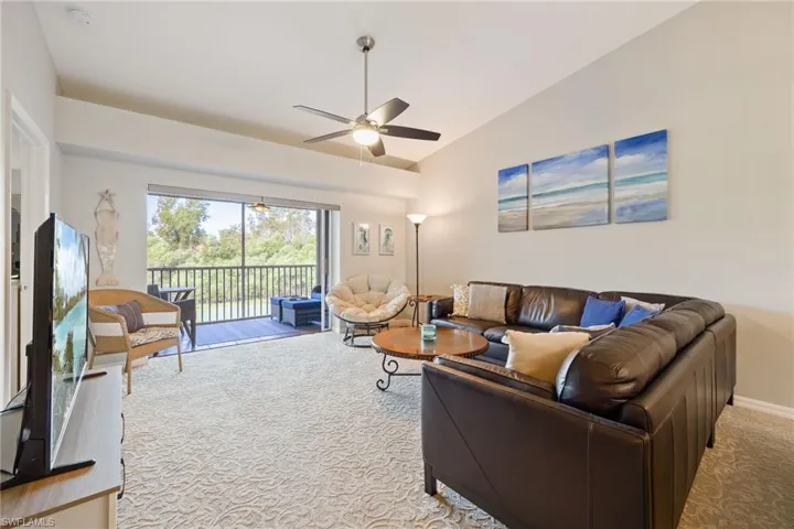 Living area with vaulted ceiling, a ceiling fan, and light carpet