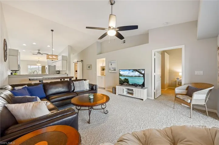 Living room featuring a barn door, ceiling fan, light colored carpet, and vaulted ceiling