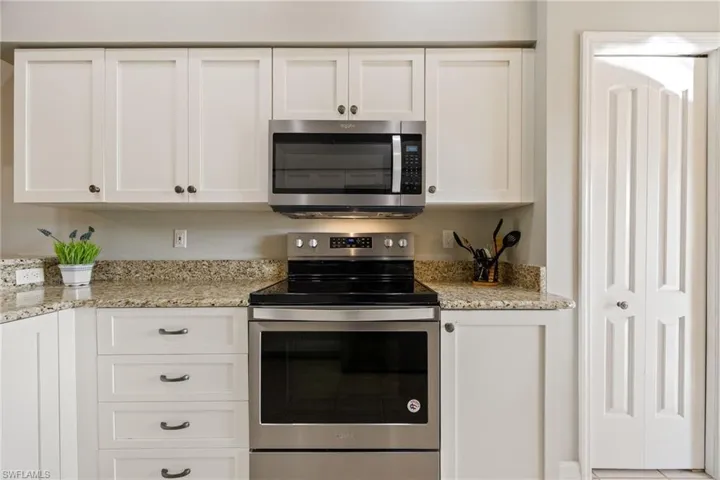 Kitchen featuring stainless steel appliances, white cabinetry, and light stone countertops