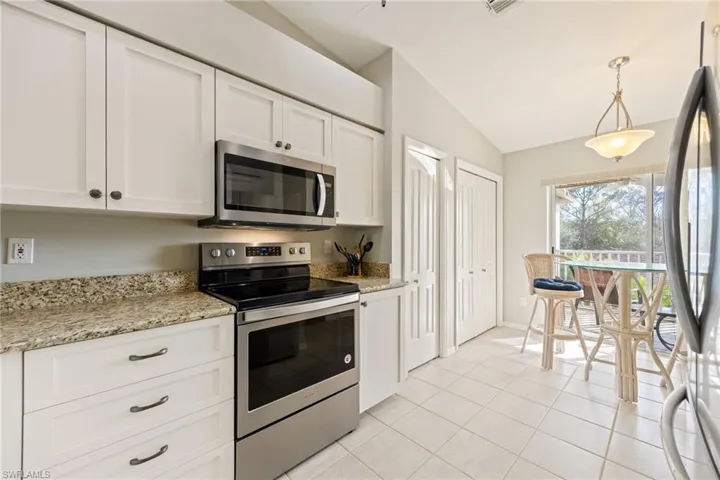 Kitchen with stainless steel appliances, white cabinetry, light stone countertops, vaulted ceiling, and hanging light fixtures