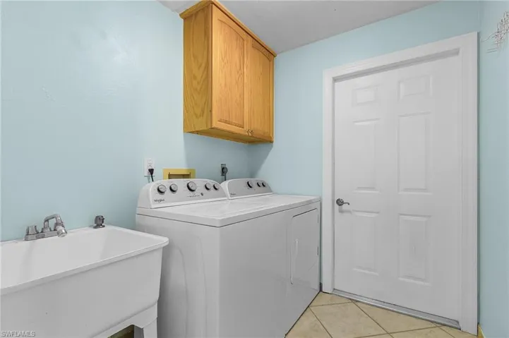 Clothes washing area featuring cabinets, independent washer and dryer, light tile patterned floors, and sink
