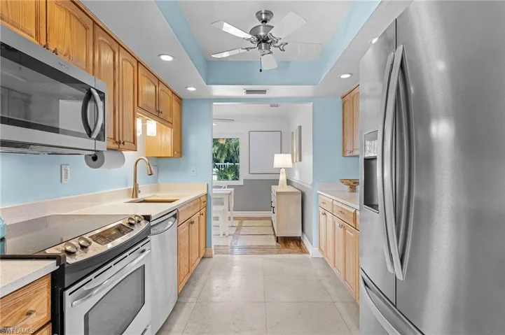 Kitchen featuring stainless steel appliances, a tray ceiling, ceiling fan, sink, and light tile patterned flooring