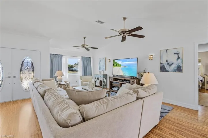 Living room with crown molding, ceiling fan, lofted ceiling, and light wood-type flooring