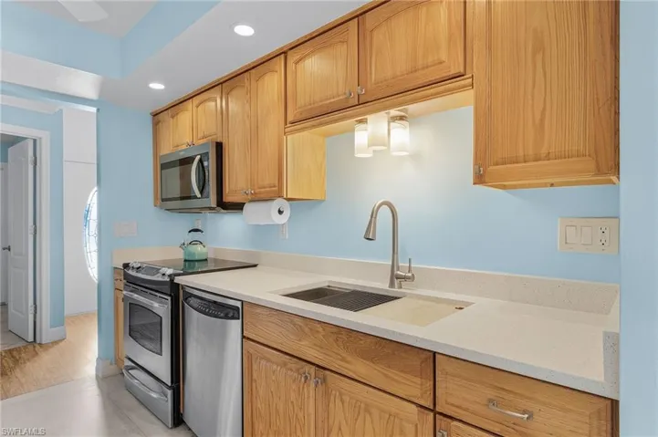 Kitchen with appliances with stainless steel finishes, light wood-type flooring, light stone counters, and sink